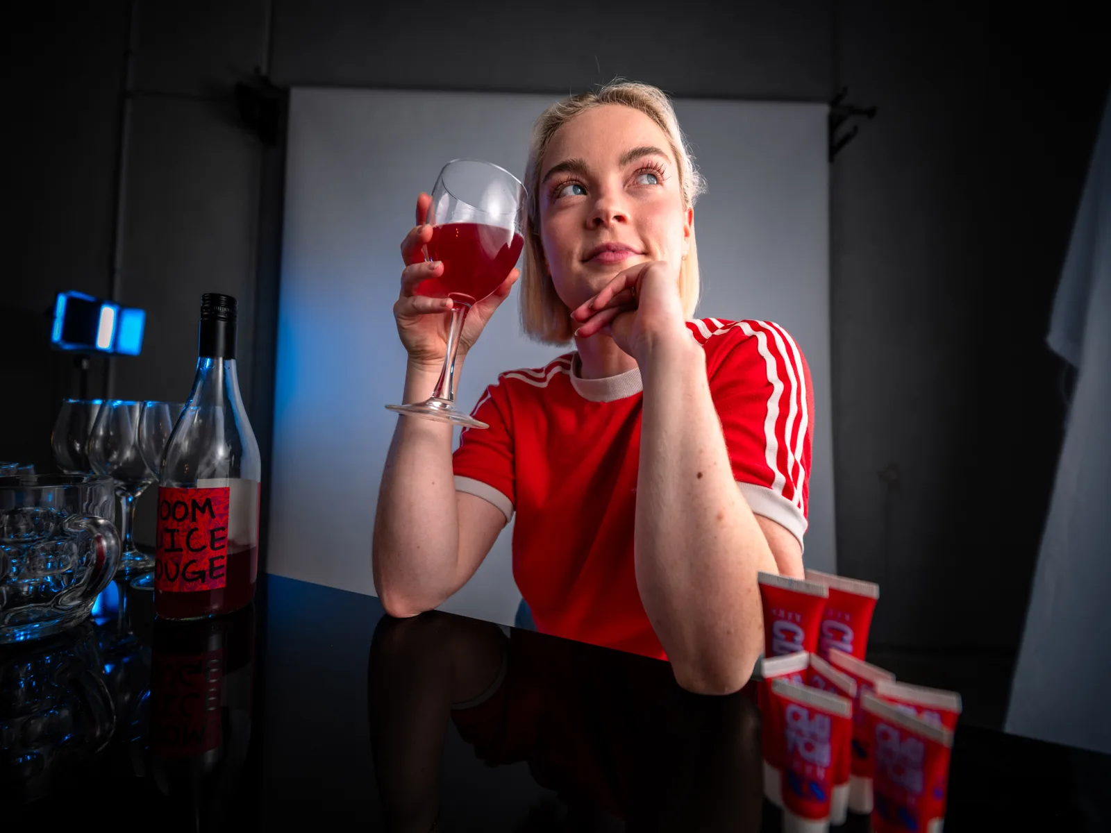 Lucy at a table raising a glass of red wine, a row of CLUTCH Glue tubes beside her