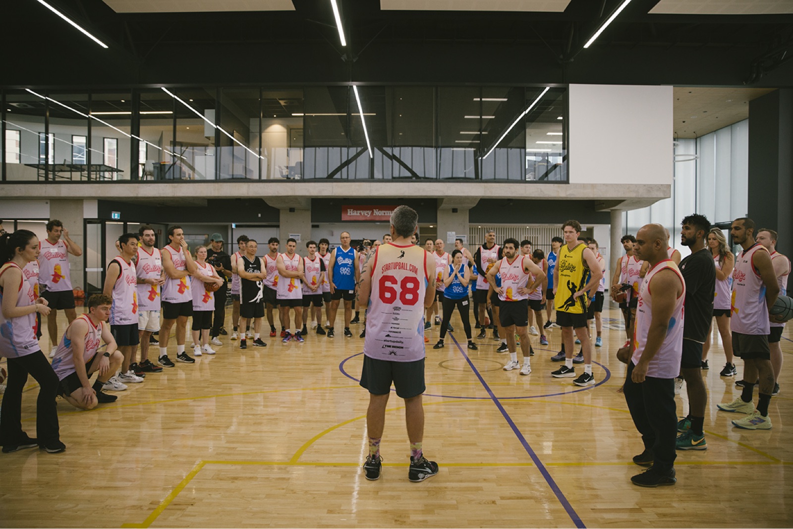 Players in pink and black singlets ringed around a court as Startup Ball is called on