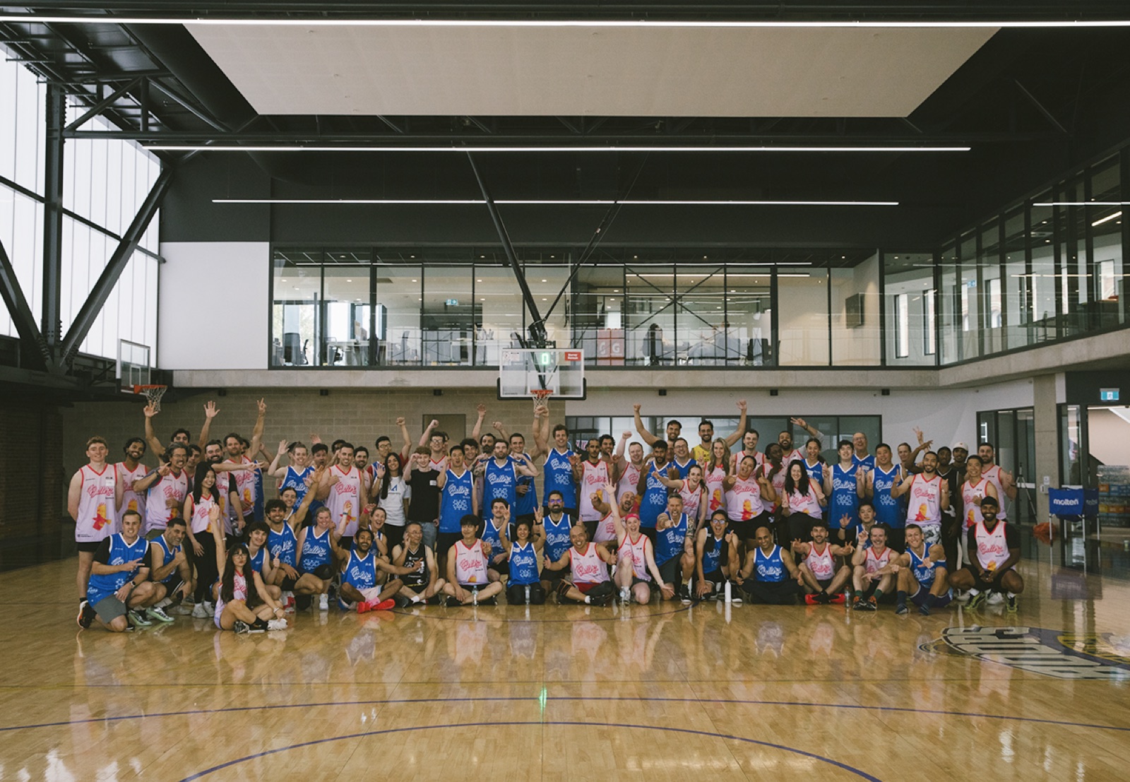 The whole Startup Ball crowd in blue and pink singlets, posed together on a basketball court